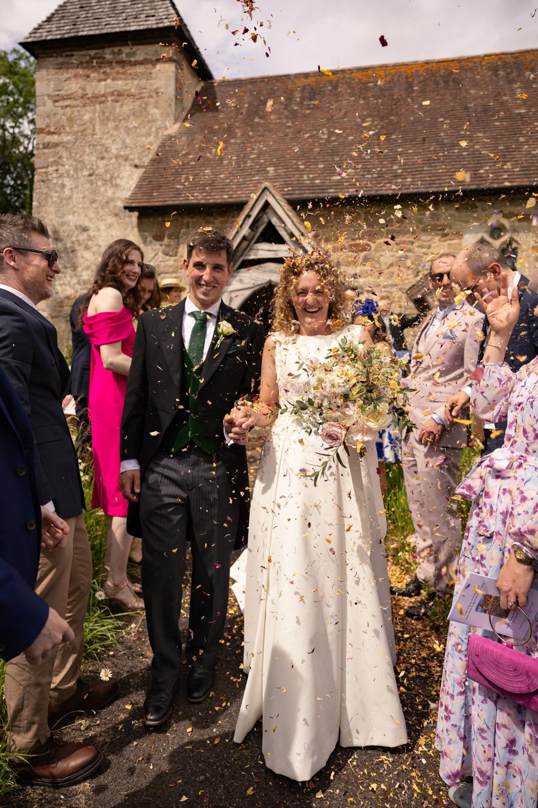 Newlyweds walking through a shower of confetti outside a country stone church