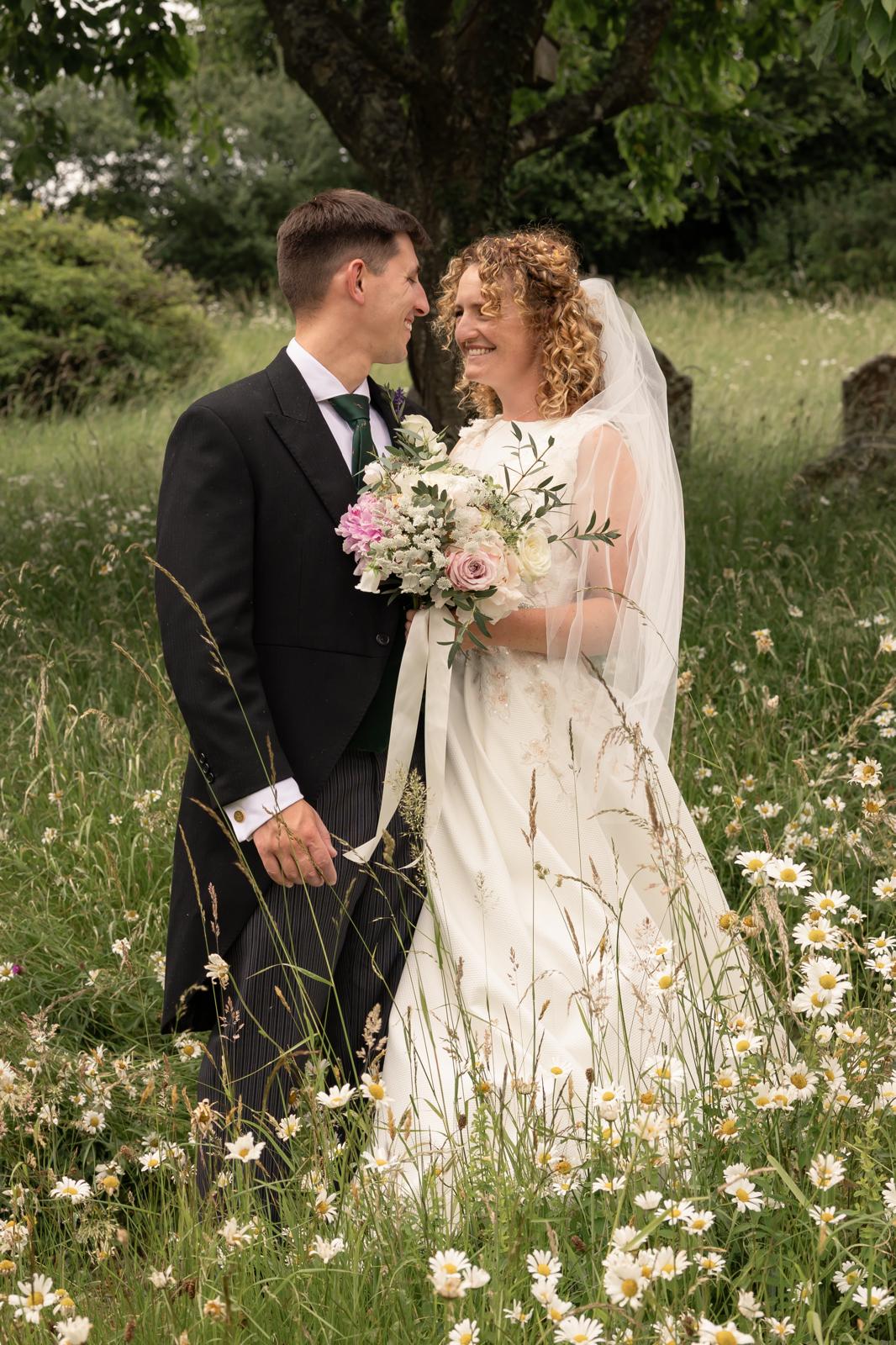Bride and groom sharing a quiet moment in a wildflower meadow of ox-eye daisies